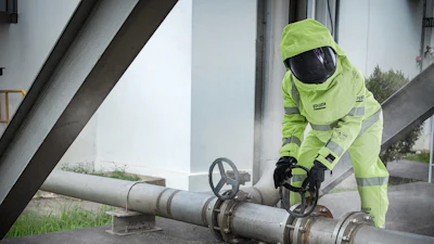 Industrial worker in neon safety gear adjusting valve on large metal pipeline system