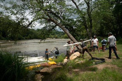 Community members assist with river rescue operations near a large tree on muddy riverbank